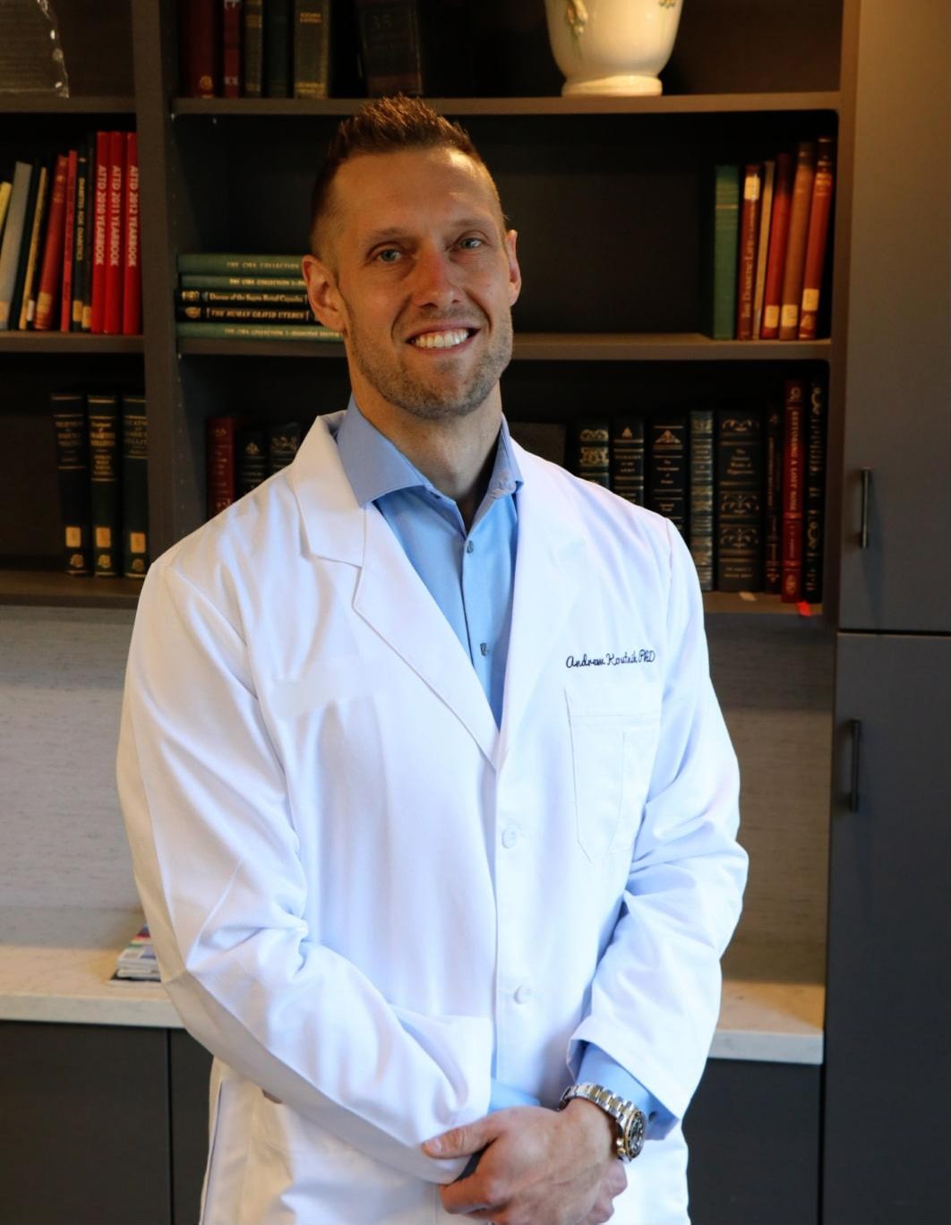 Dr. Andrew Koutnik in a white coat in front of a bookshelf